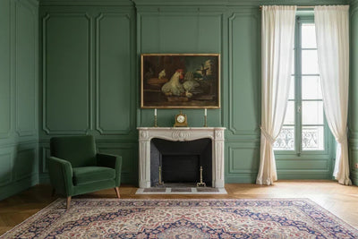 Wide antique painting hung above a marble mantel in a green panelled French sitting room