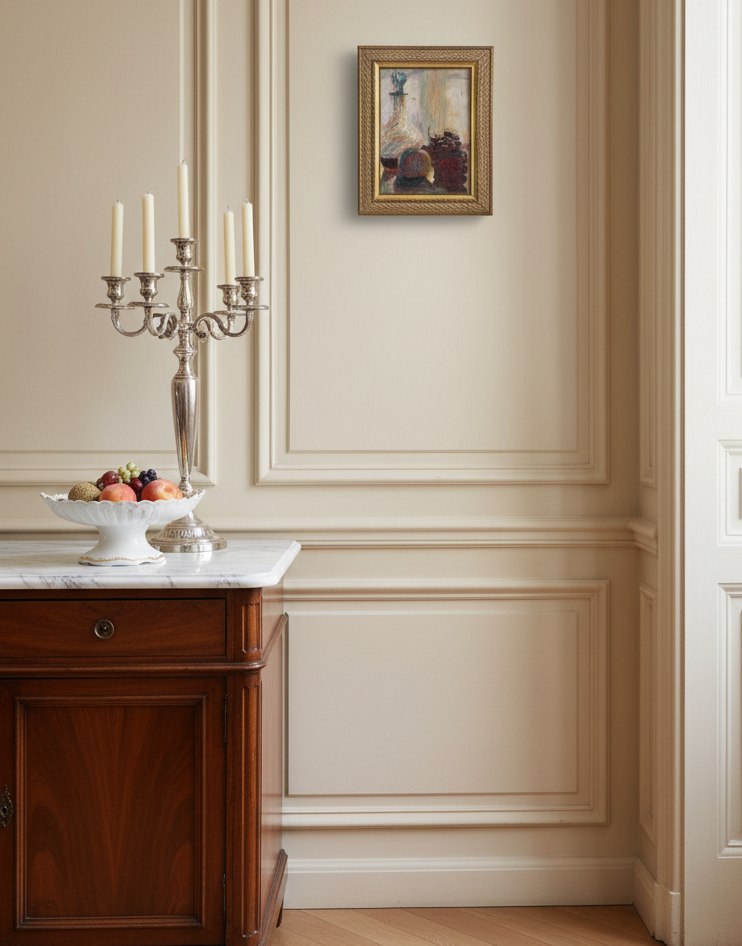 The framed still life hanging on a cream panelled wall above a marble-topped sideboard with a silver candelabra and a fruit stand