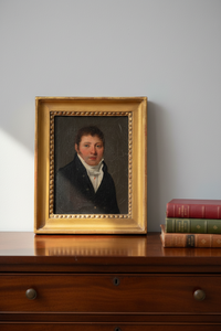 The portrait stands upright on a mahogany chest, no taller than the three books stacked beside it
