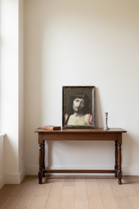 The Ecce Homo in its ebonised frame resting on an oak side table in a plain white room, showing the scale of the framed canvas