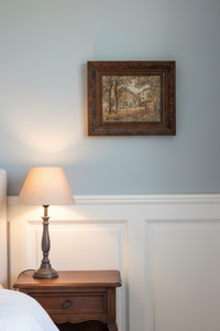 The framed painting hanging above a walnut bedside table with a lamp, on a pale blue-grey wall with white panelling